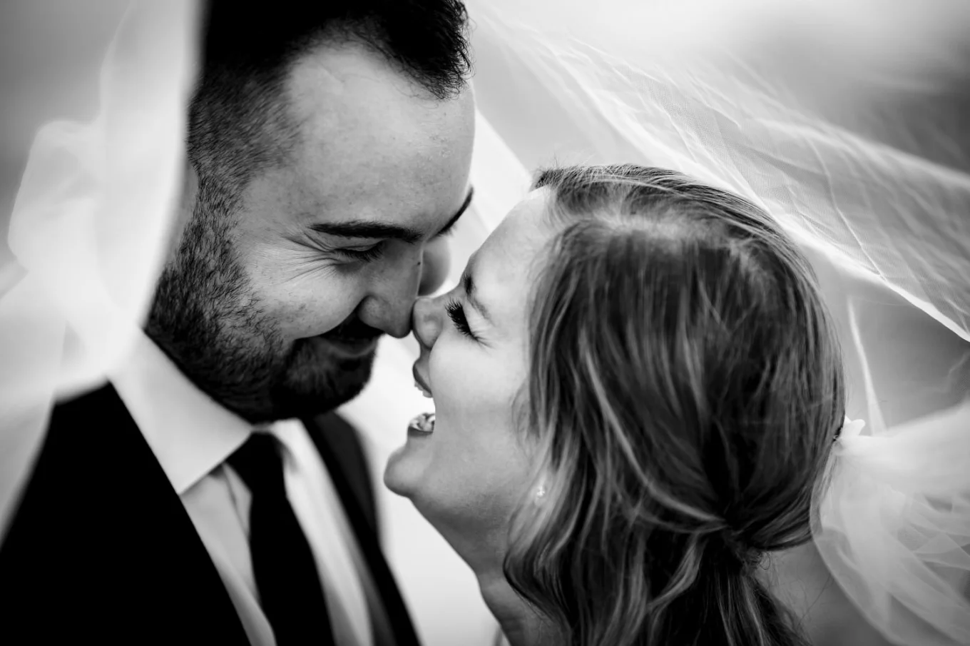 Bride and groom under the veil. They laugh and look deeply info each others eyes.