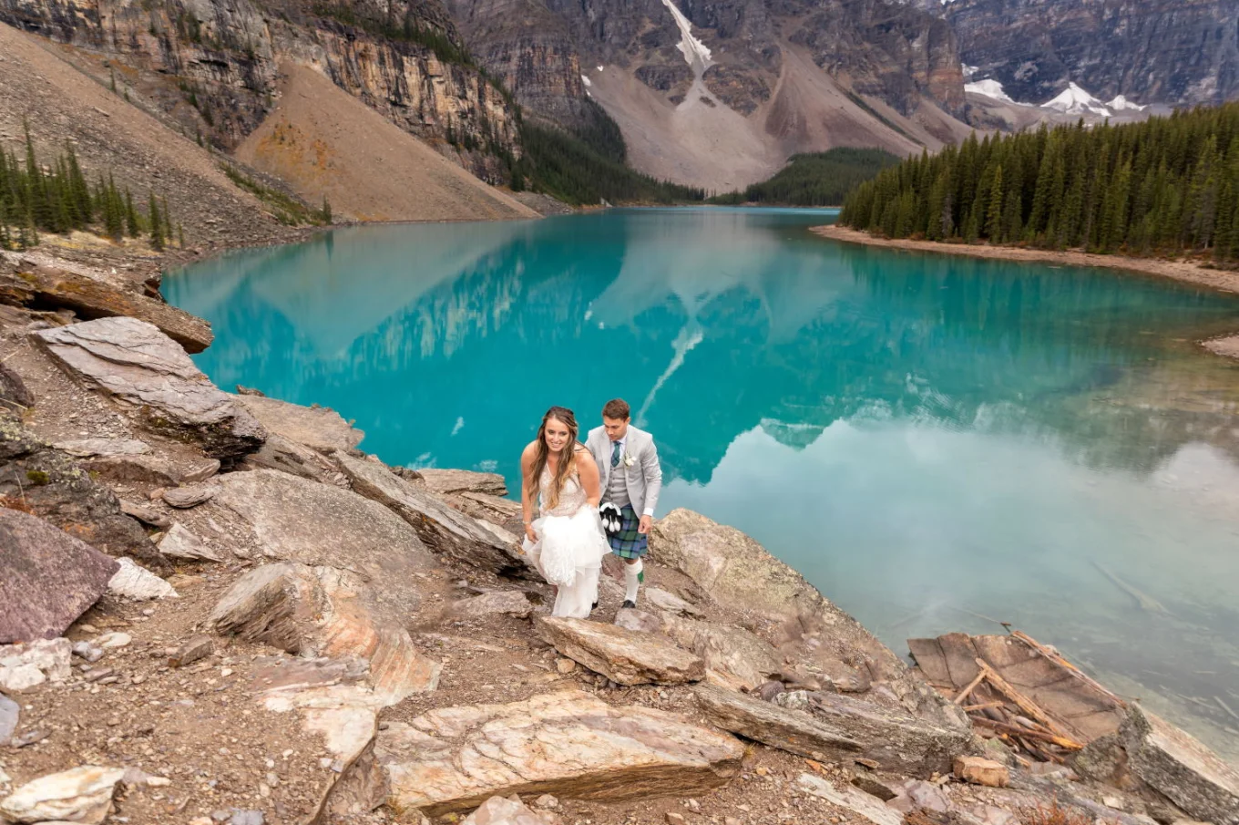 Groom holding the bride's wedding dress while climbing the mountain after wedding ceremony