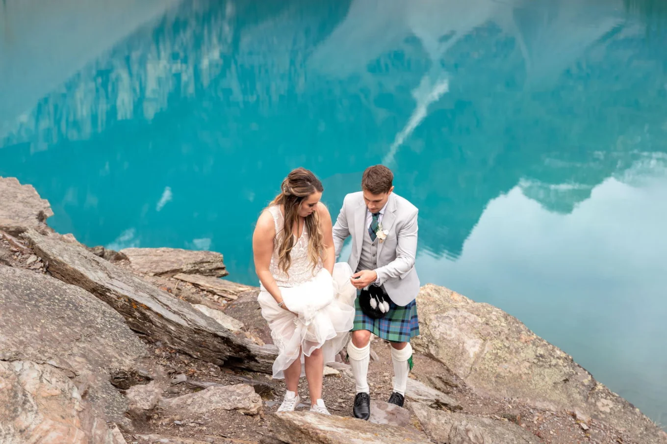 Scottish groom taking care of his wife's wedding dress while going up the hill after their elopement at Moraine Lake