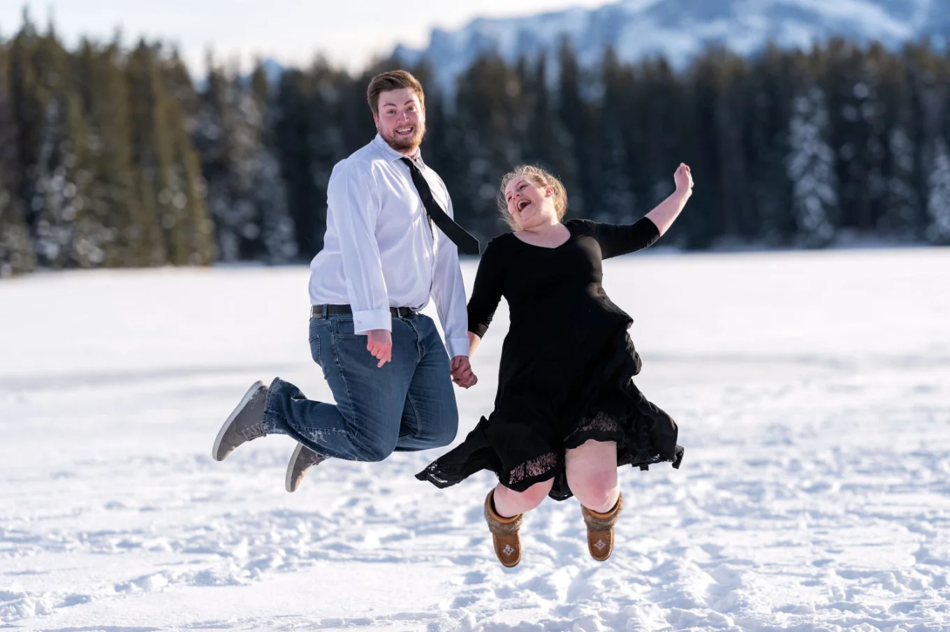 Happy couple in love jumps at the frozen Two Jack Lake in Banff.
