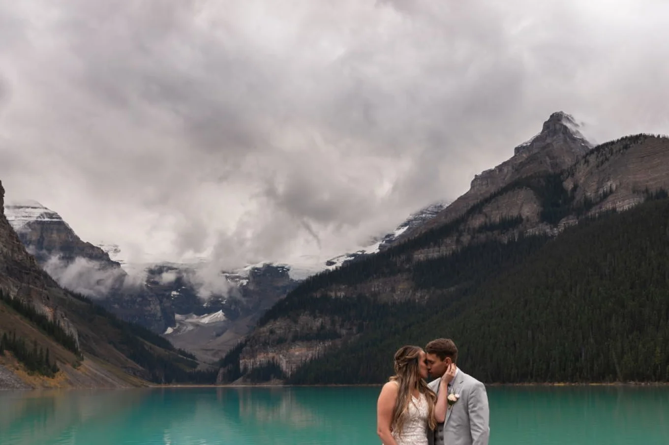 Beautiful bride kissing her new husband at Lake Louise which is surrounded by the mountains