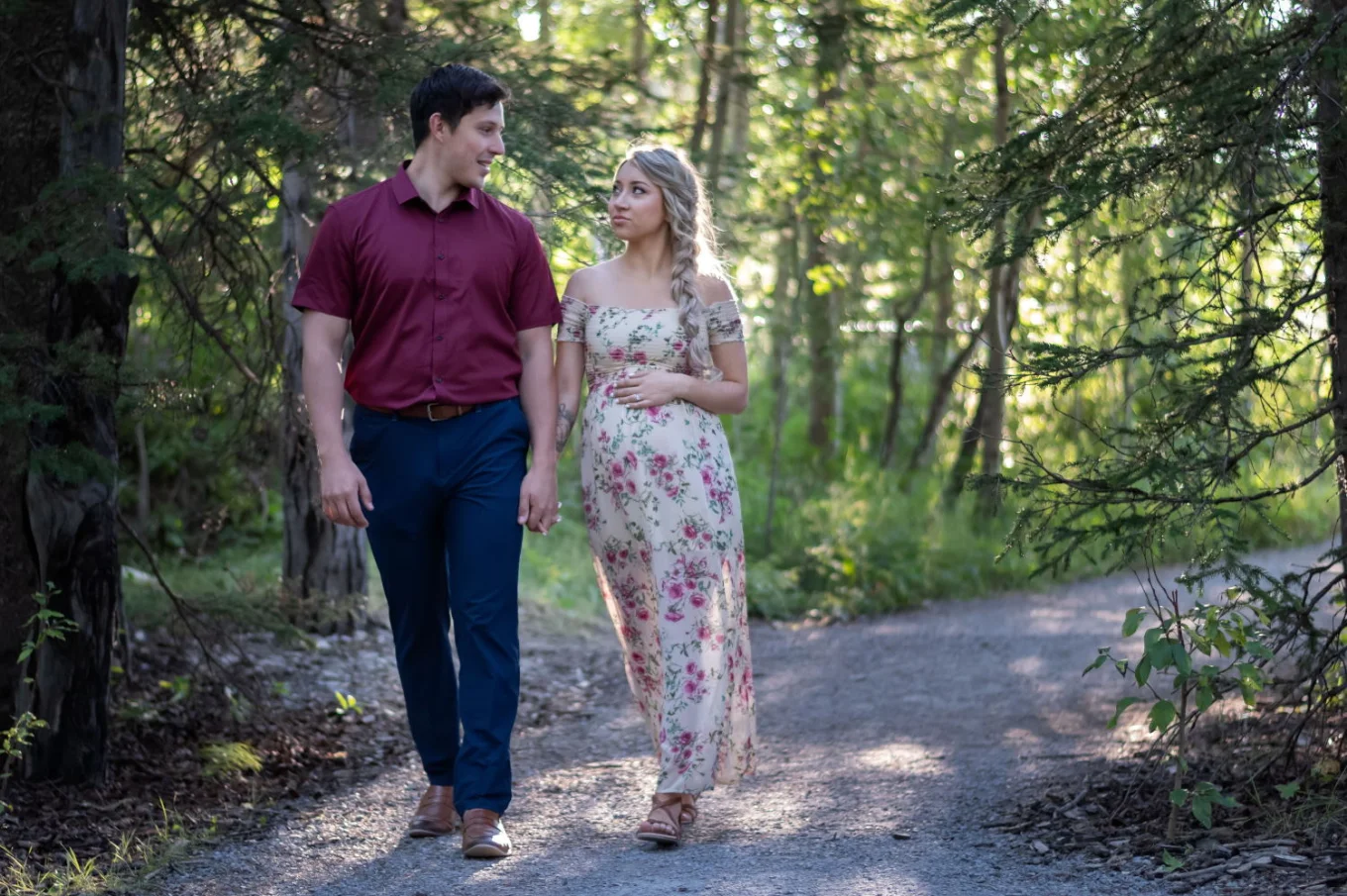 Future parents walking in forest in Banff. They look at each other. Pregnant woman touches her belly.