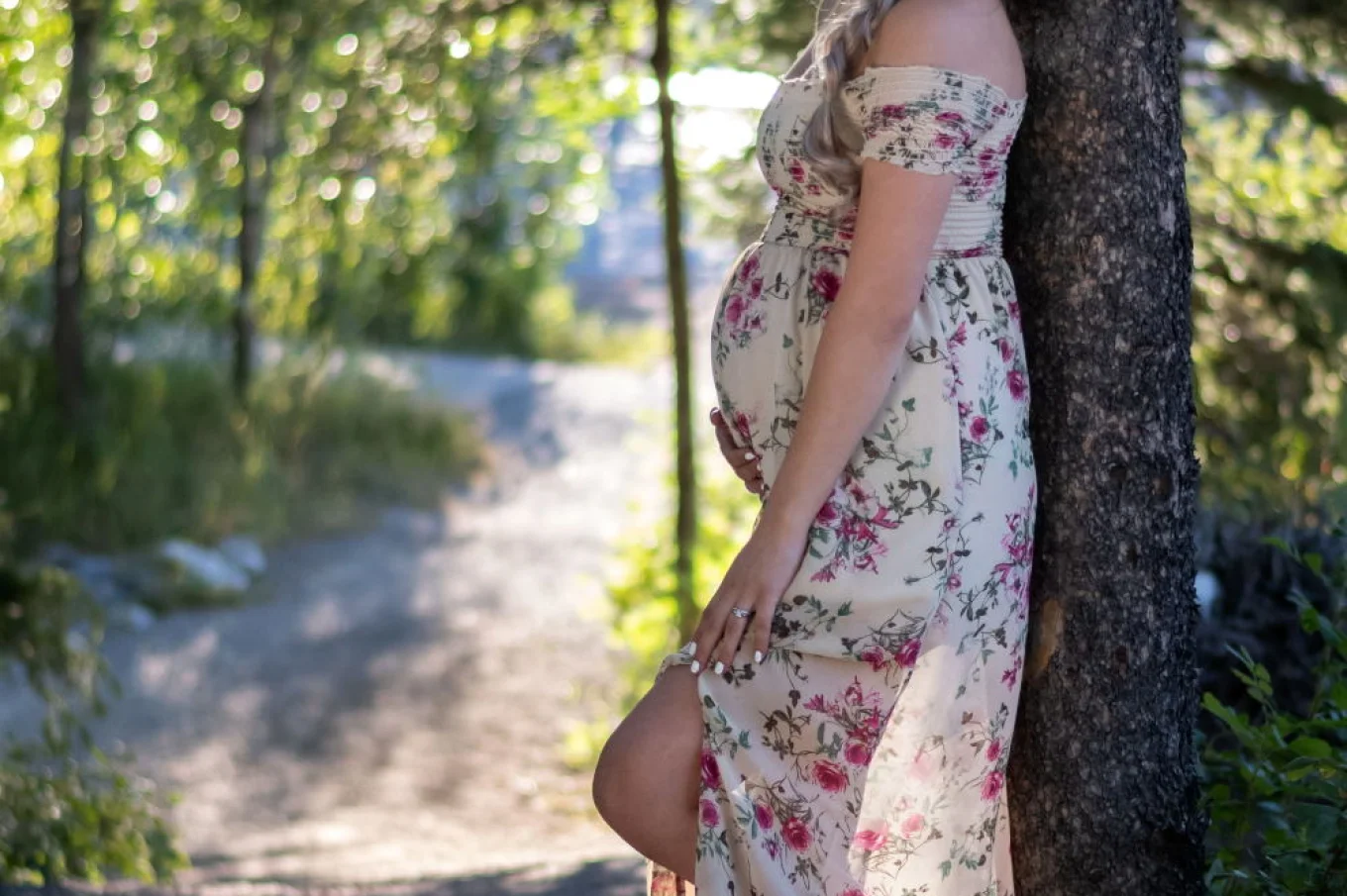 Pregnant woman posing during materning photo shoot in Banff. She lean against the tree and touch her belly.