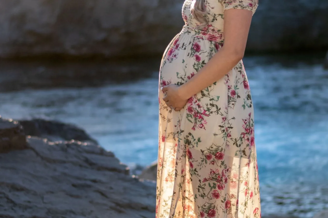 Maternity portrait in Banff. Pregnant woman touches her bally and smiles at the camera.