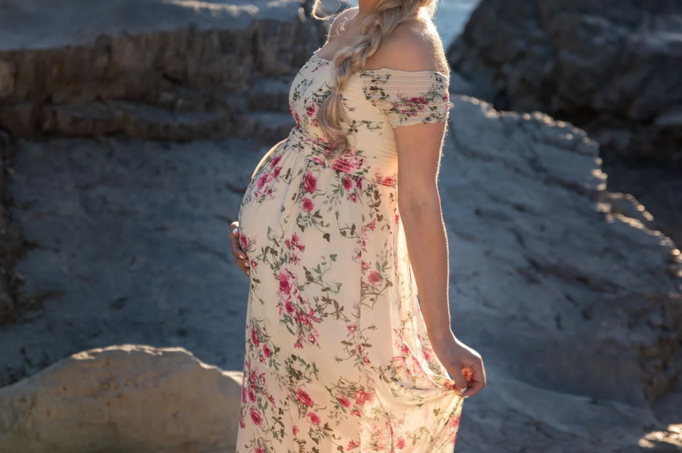Proud pregnant woman touches her belly and smiles at the camera during maternity photo session in Banff.