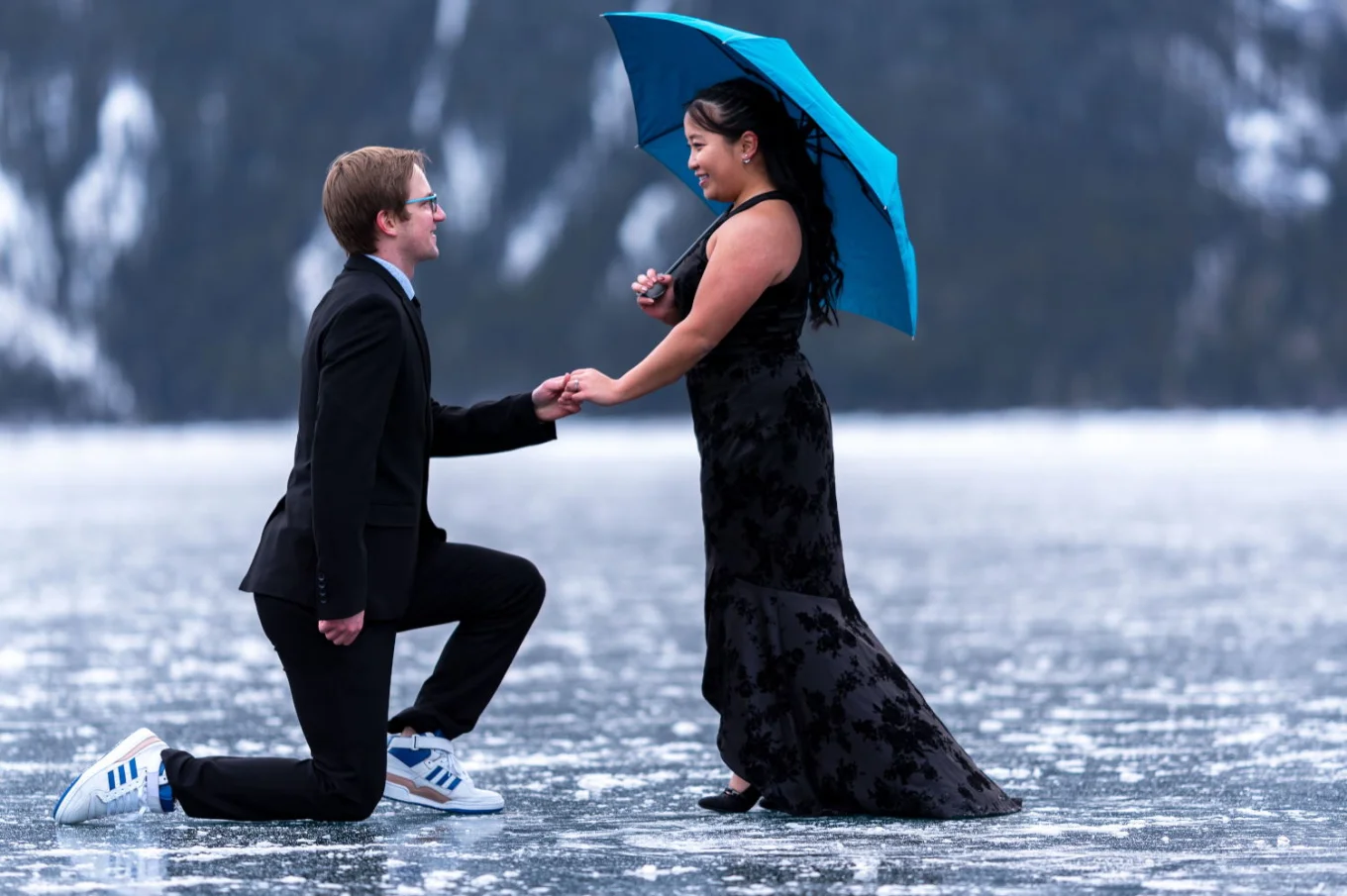 Romantic proposal on one knee in Banff. Future bride cover herself under a blue umbrella.