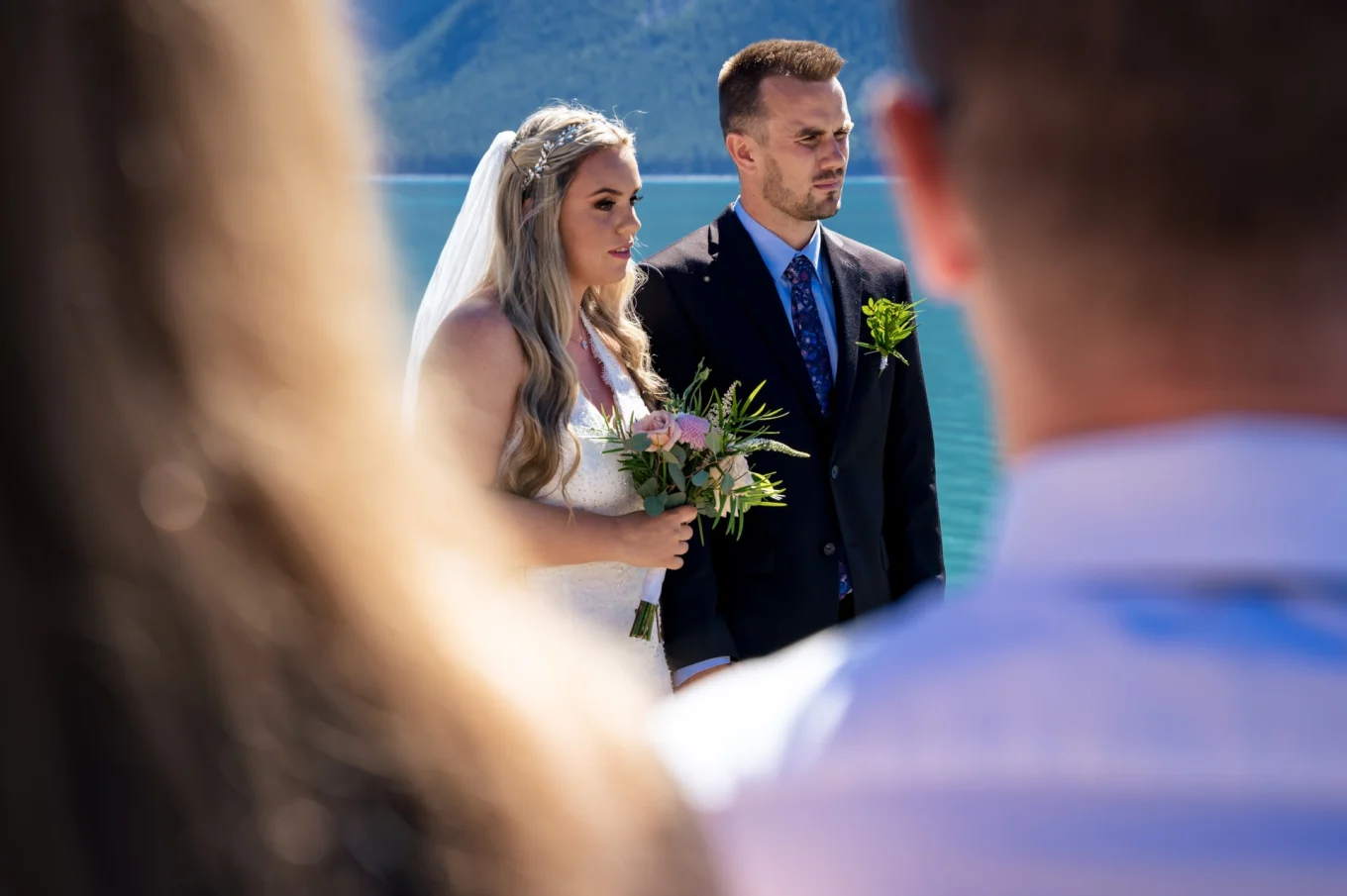 Elopement ceremony at Minnewanka Lake . Bride and groom listening Pastor's speech.