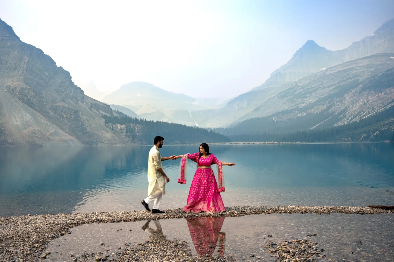 Indian engaged couple is dancing at Bow Lake. They are wearing traditional outfit in pink and gold colors.