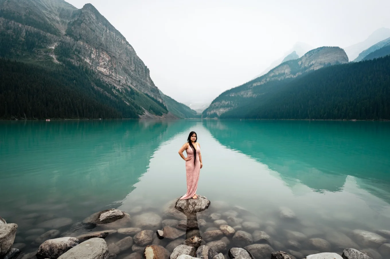 Woman in a pink long dress is standing on the rock at the Lake Louise. She is posing for Banff Wedding Photographers.