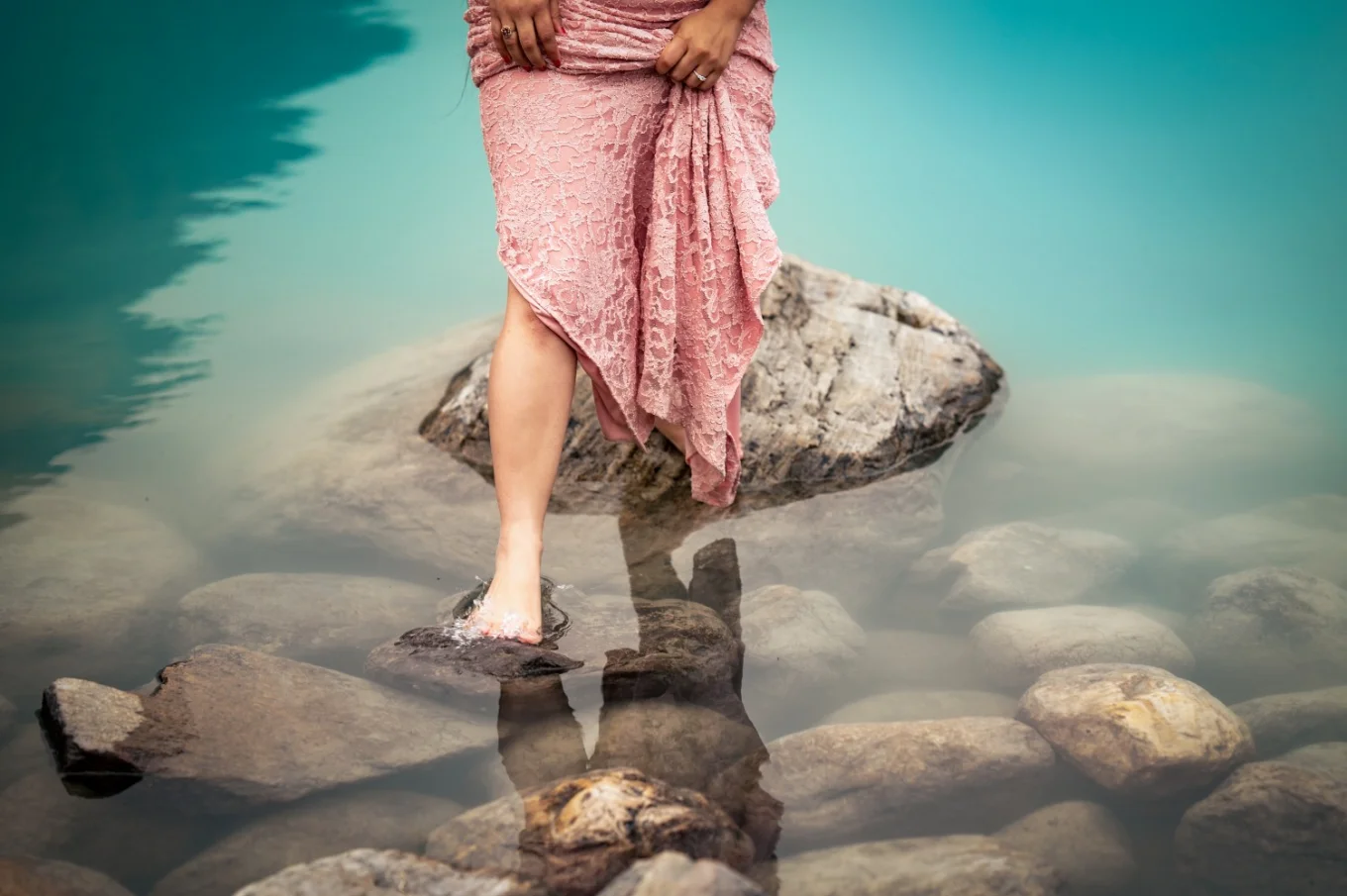 Woman in pink dress is jumping from the rock at Lake Louise. She is barefoot.