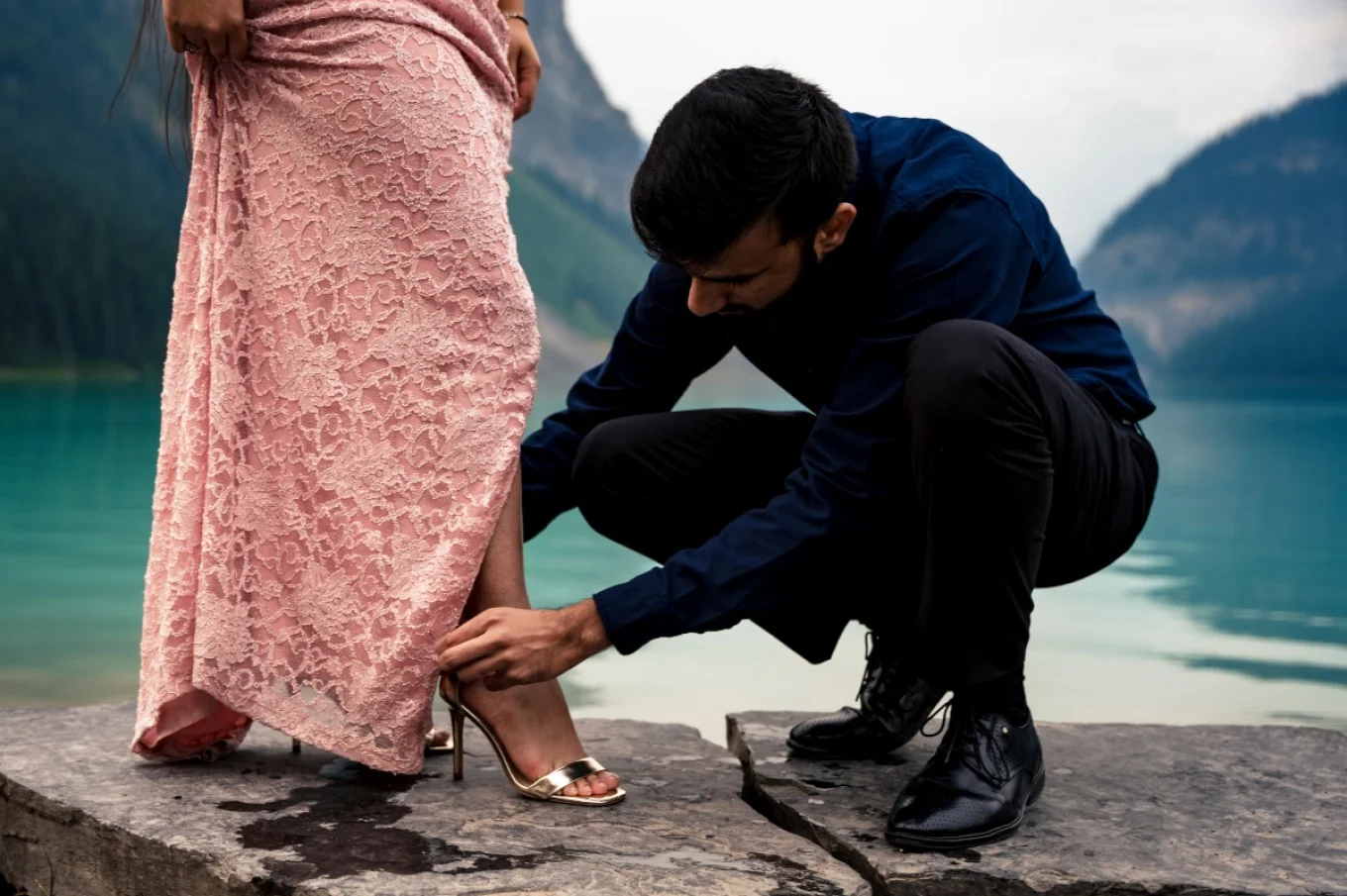 Indian man helping his fiancé to fixing her shoes before their engagement session at Lake Louise