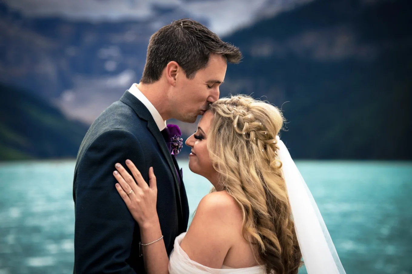 Groom is kissing the bride at the forehead.