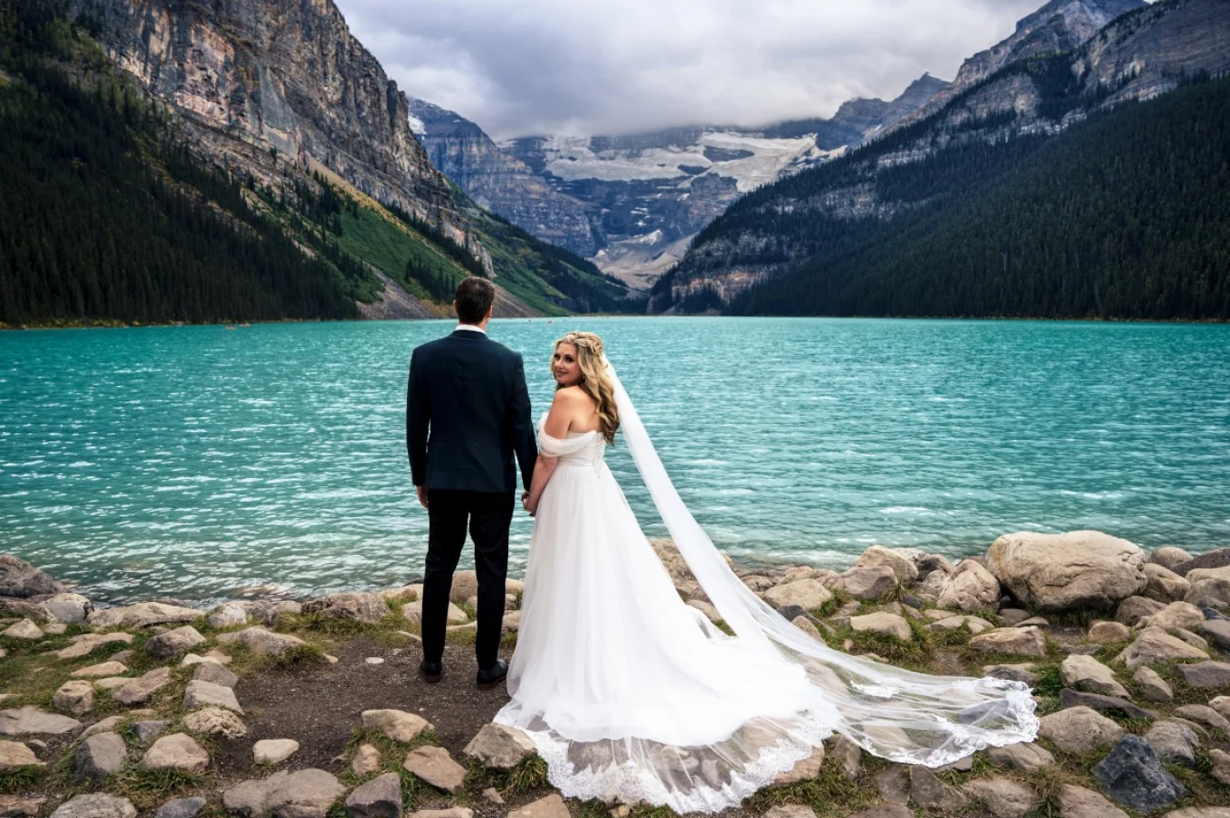 Newlyweds portrait taken at Banff Wedding. Bride looks at the camera, groom admire stunning view at Lake Louise.