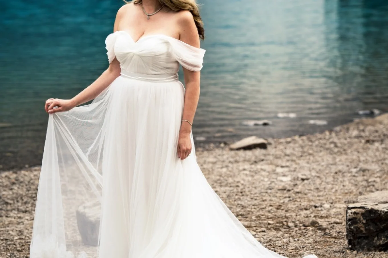 Bride's portrait taken by the Lake. She looks ahead holding her dress.