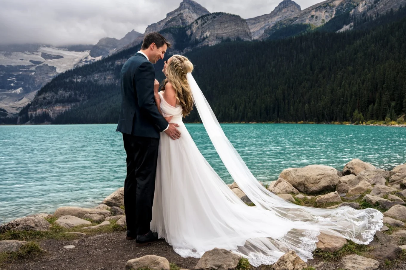 Bride and groom portrait by the Lake Louise. Couple look deeply on each other.