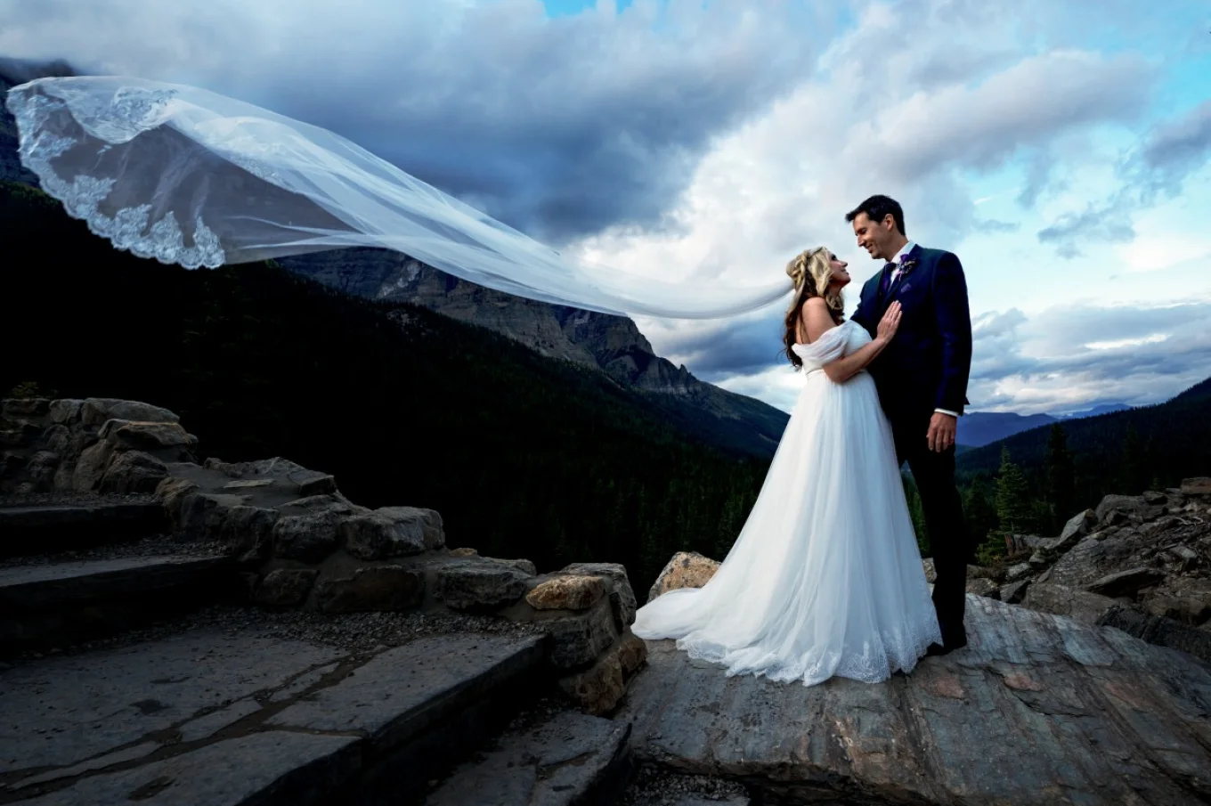 Adventures newlyweds standing at the rock and looking at each other. Bride's veil is blown by air.