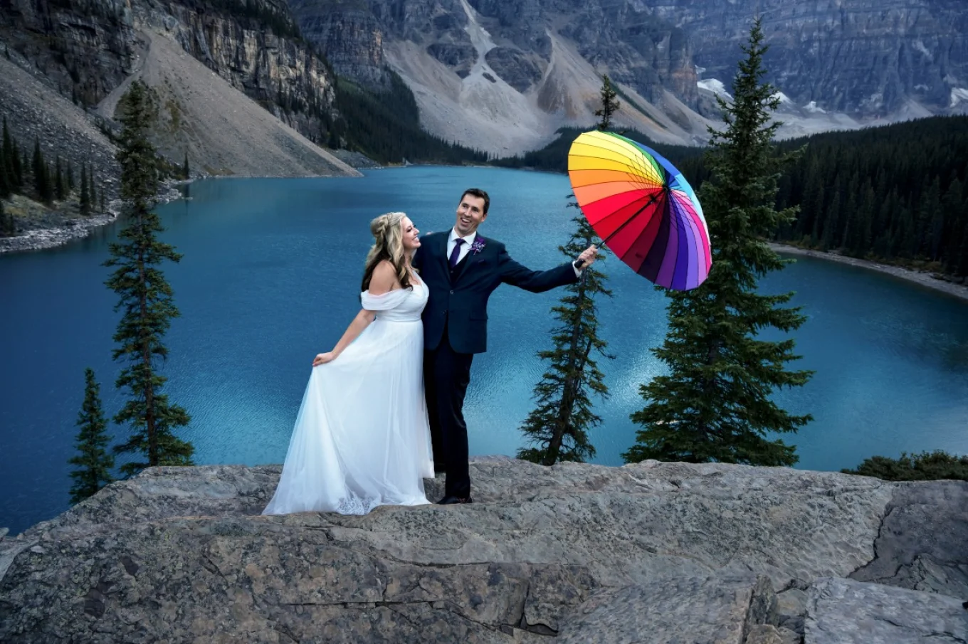 Groom try to hold colourful umbrella. Wind is strong and the umbrela is alms blown away. Amused bride looks at her husband.