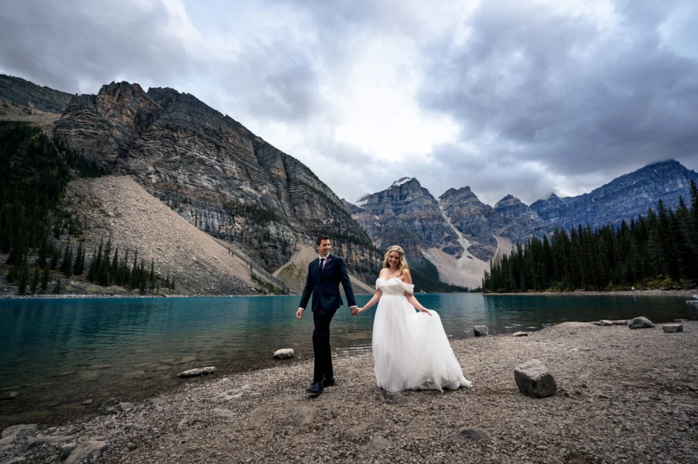Wedding photo session at Moraine Lake captured by Banff Wedding photographer. Newlyweds walk down the lake and holds their hands.