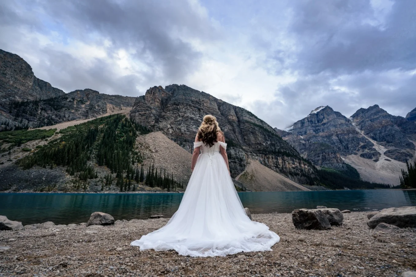 Bride wears long and white wedding dress. She look forward at the Canadian Rockies in Banff.