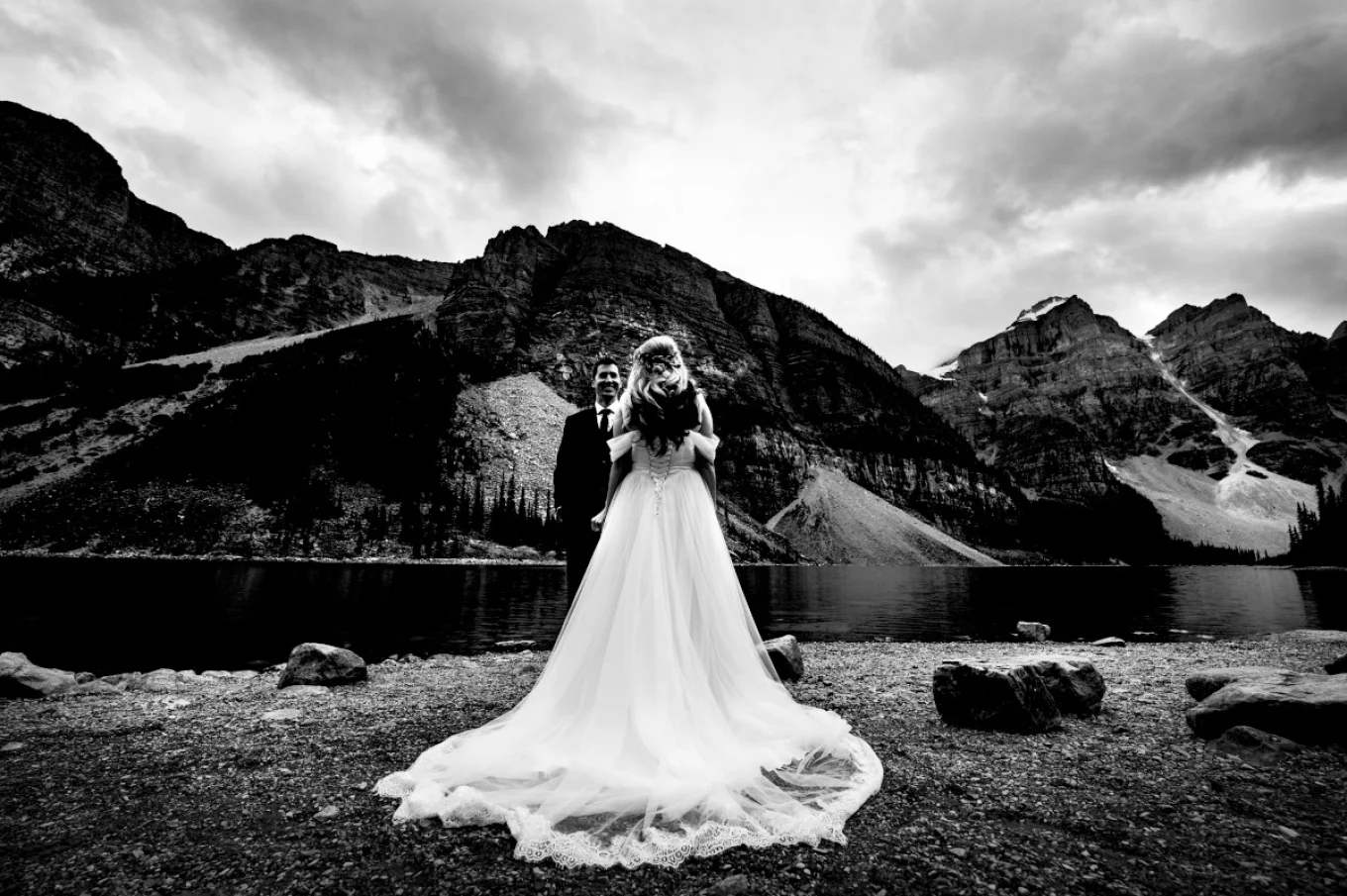 Black and white photograph of newlyweds. Bride wears long stunning dress. Groom admire her beauty.