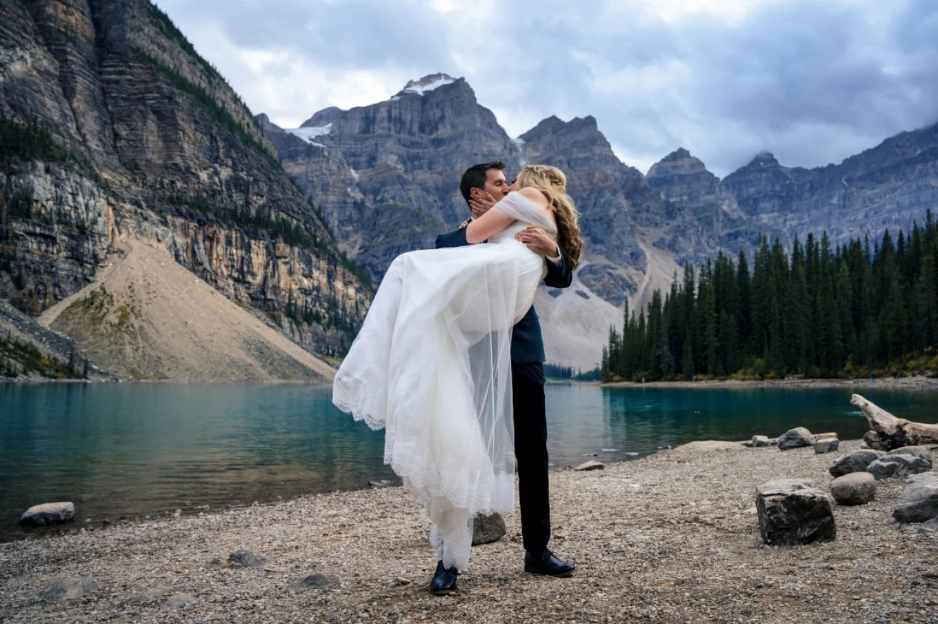 Groom holds the bride on his hands. They are kissing surrounded by the Canadian Rockies in Banff.