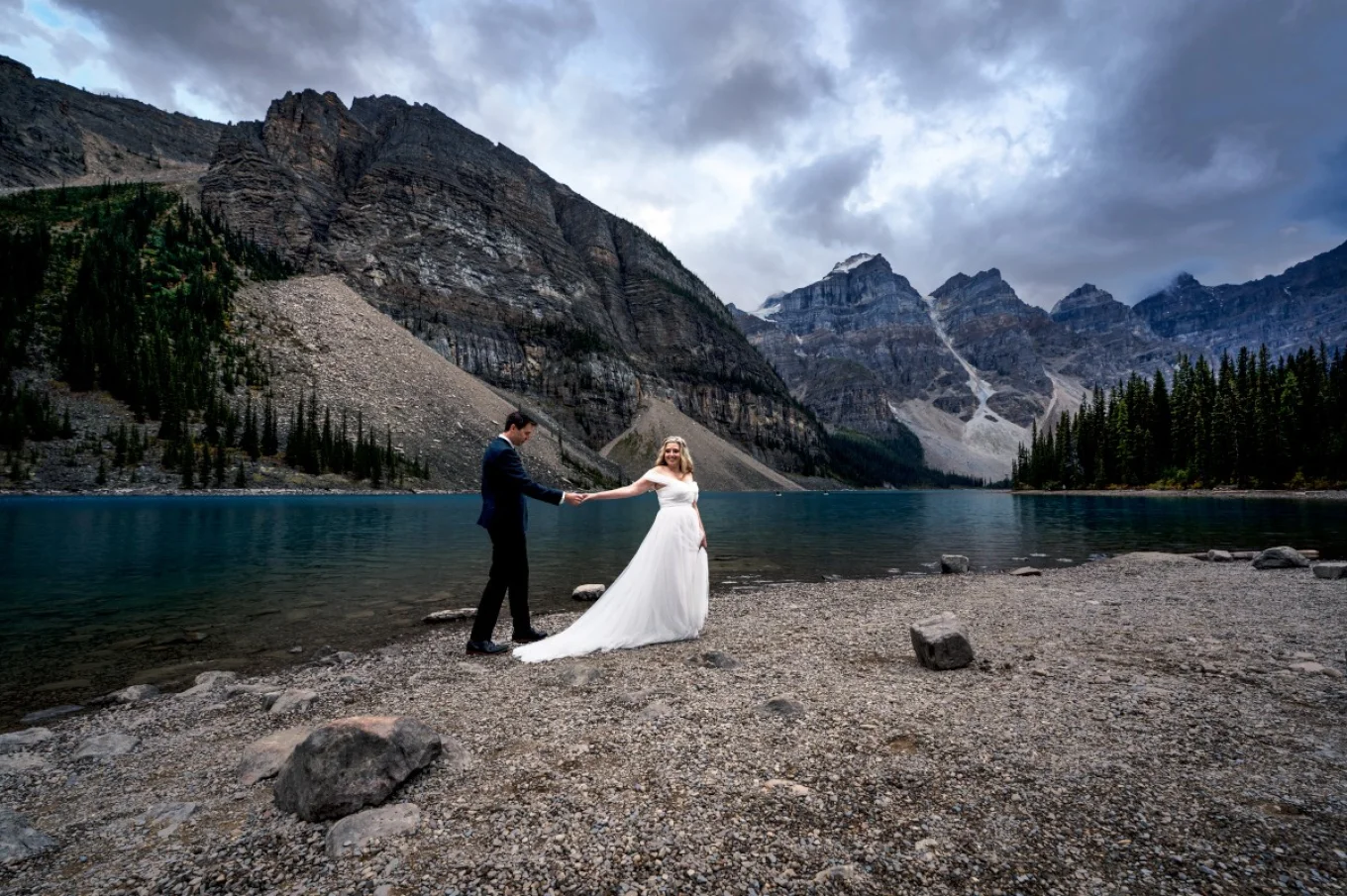 Newlyweds walk down the Moraine Lake. They holds their hands.