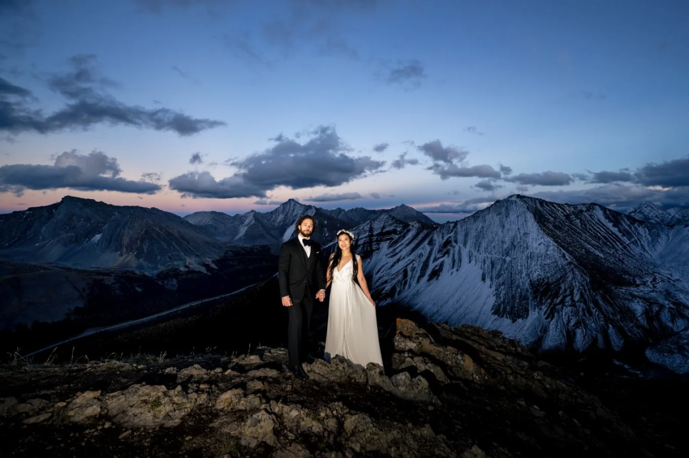 Fearless wife and husband posing at the top of the mountain in Banff .