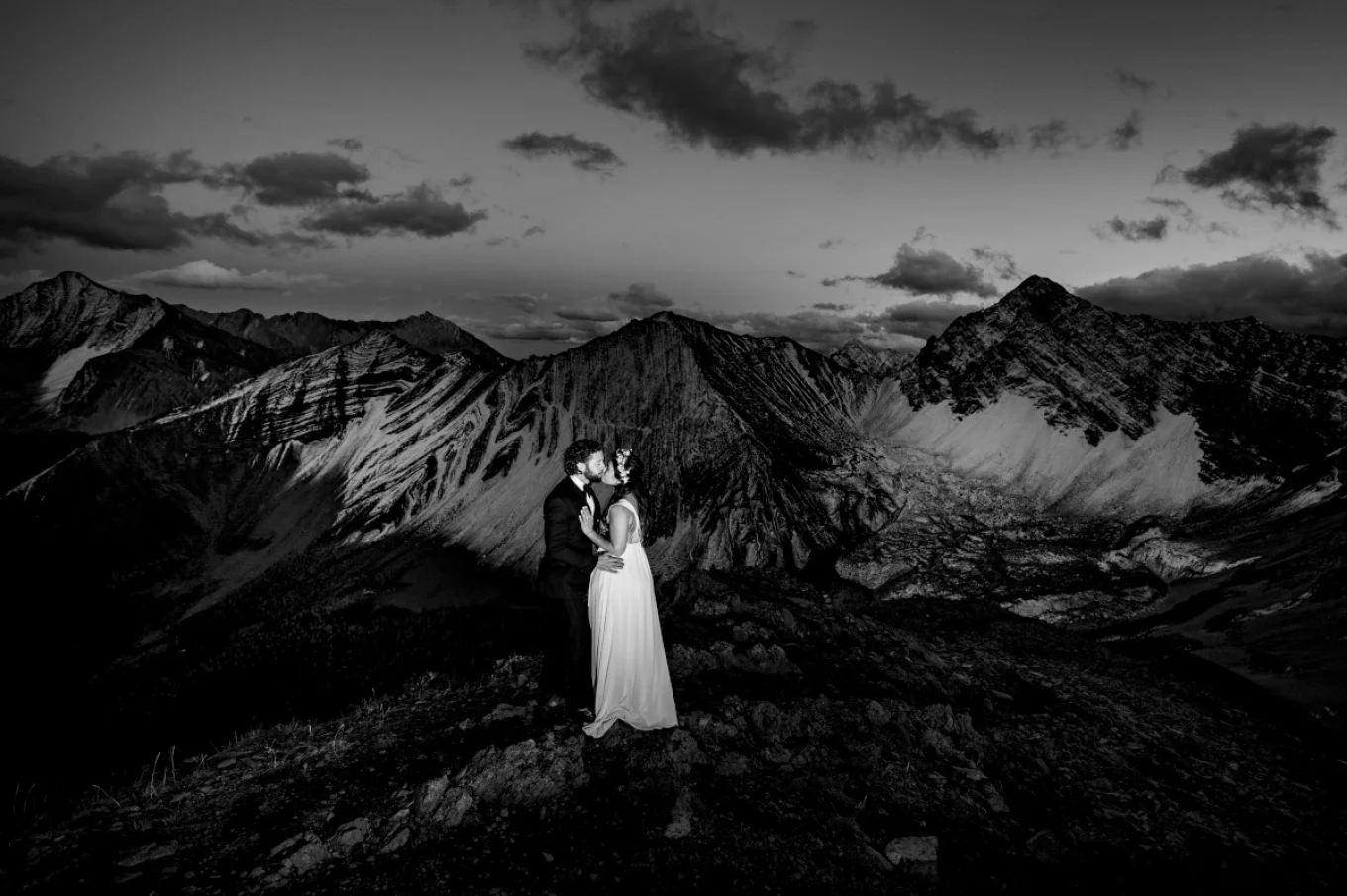 Newlyweds kissing on the peak of the Canadian Rockies while Banff Wedding Photographer capture unique moments.