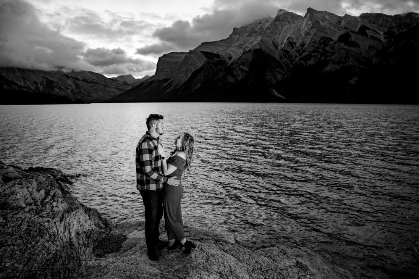 Banff Wedding Photographer caotured newly engaged couple looking at each other with love. They are at the lake surrounded by the Canadian Rockies.