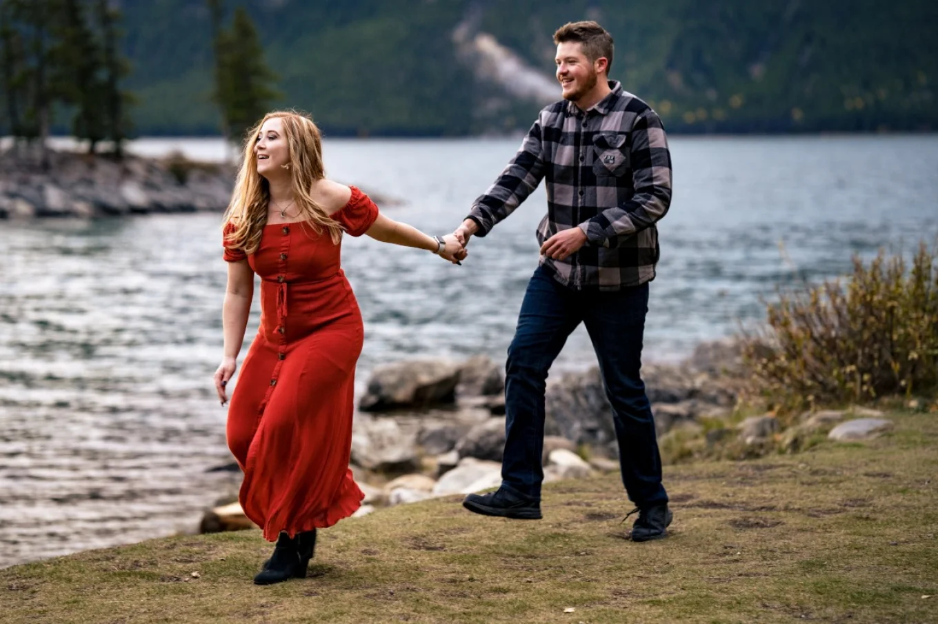 couple in love run and have fun at Minnewanka Lake in Banff. They hold their hands and laugh.