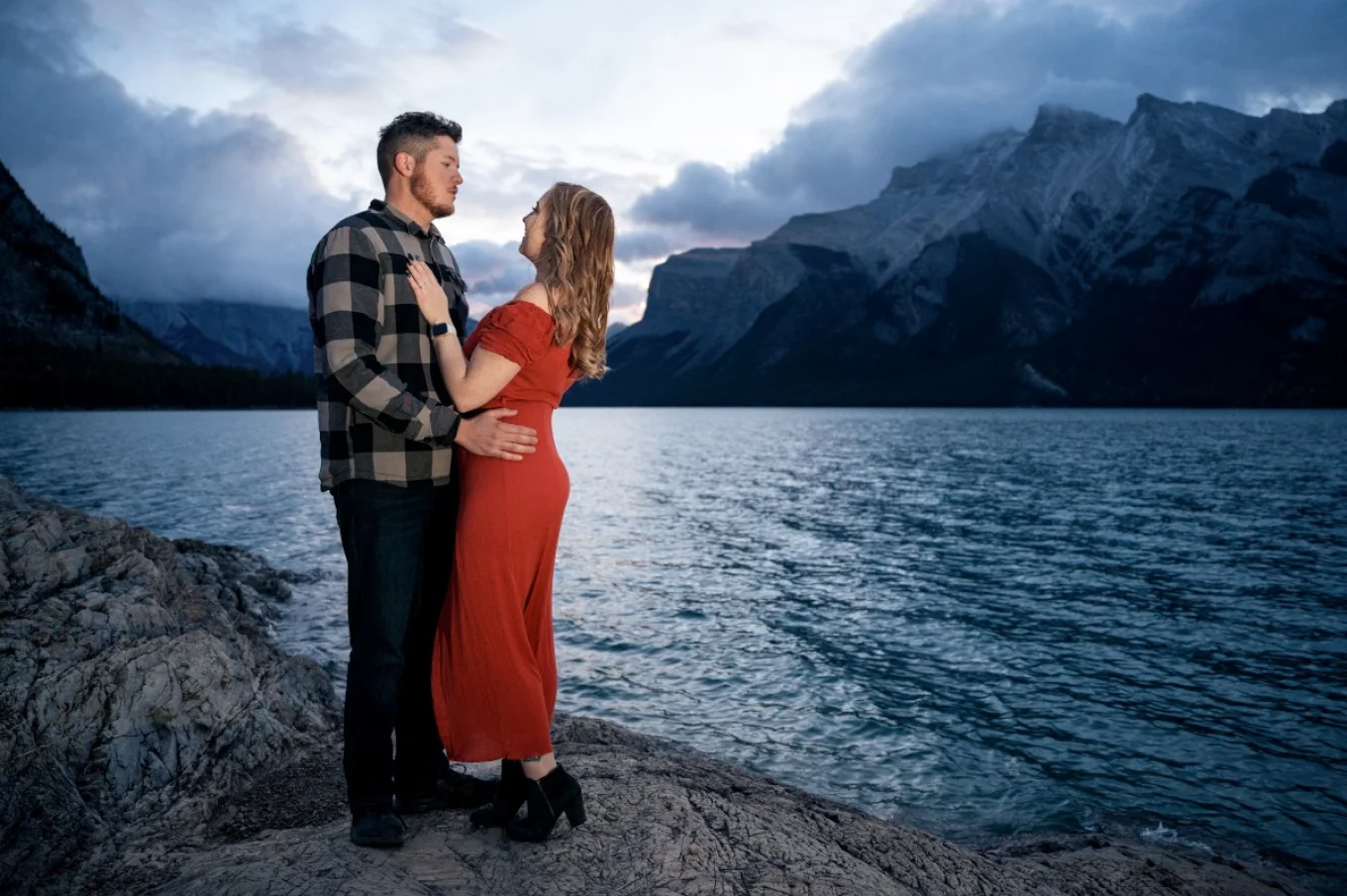 Engagement photo session taken by Calgary Wedding Photographer. Couple in love are hugging at look at each other. They are at the Minnewanka Lake in Banff.