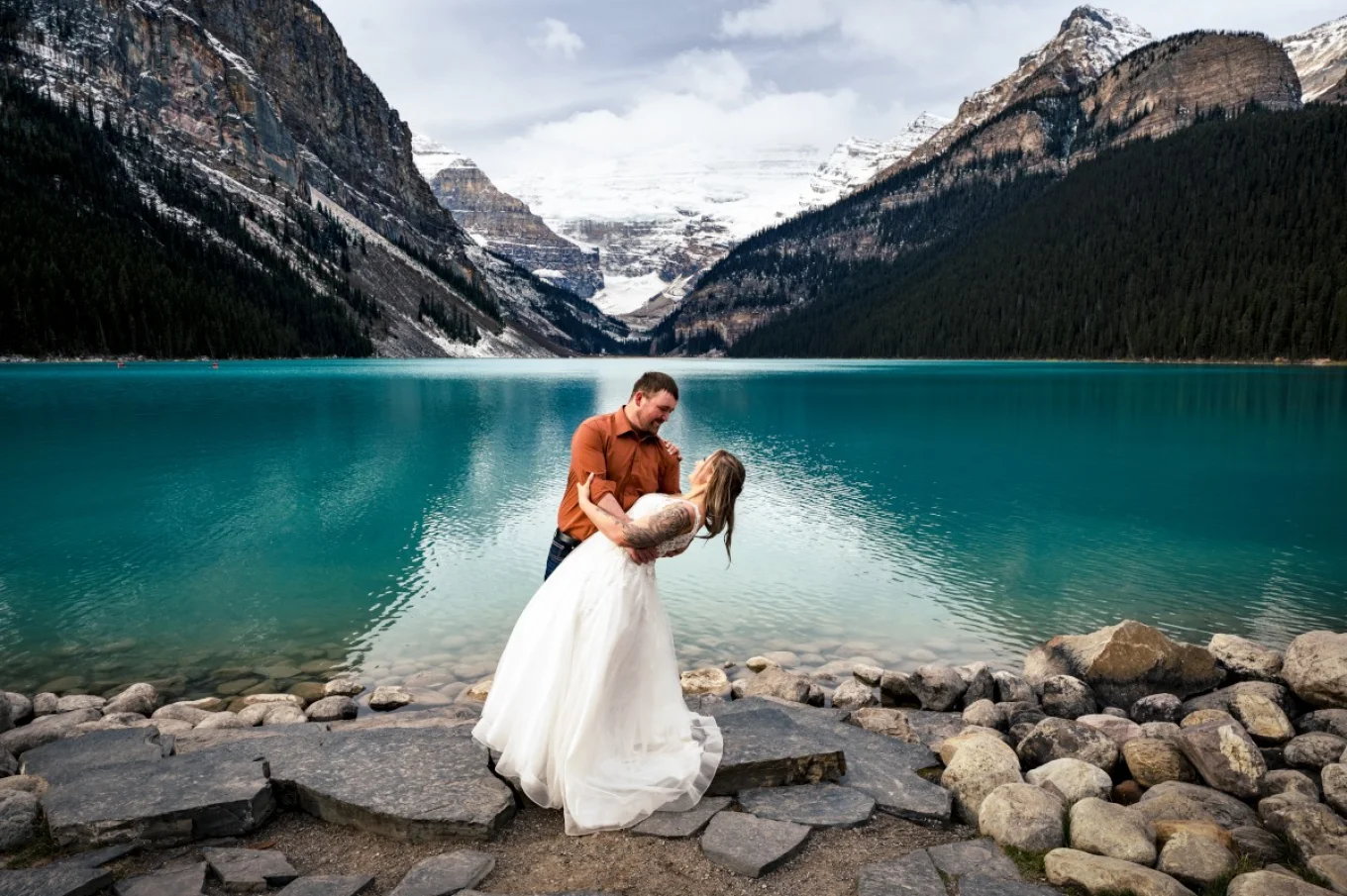 Happy newlyweds celebrate their love by dancing at Lake Louise. Lake Louise is turquoise and stunning.