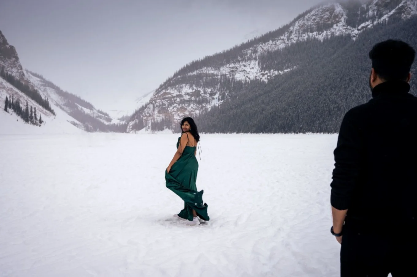 Lady dance and look charming at her husband. She dances on the frozen lake which is covered with snow. Behind her ate the Canadian Rocky Mountains.