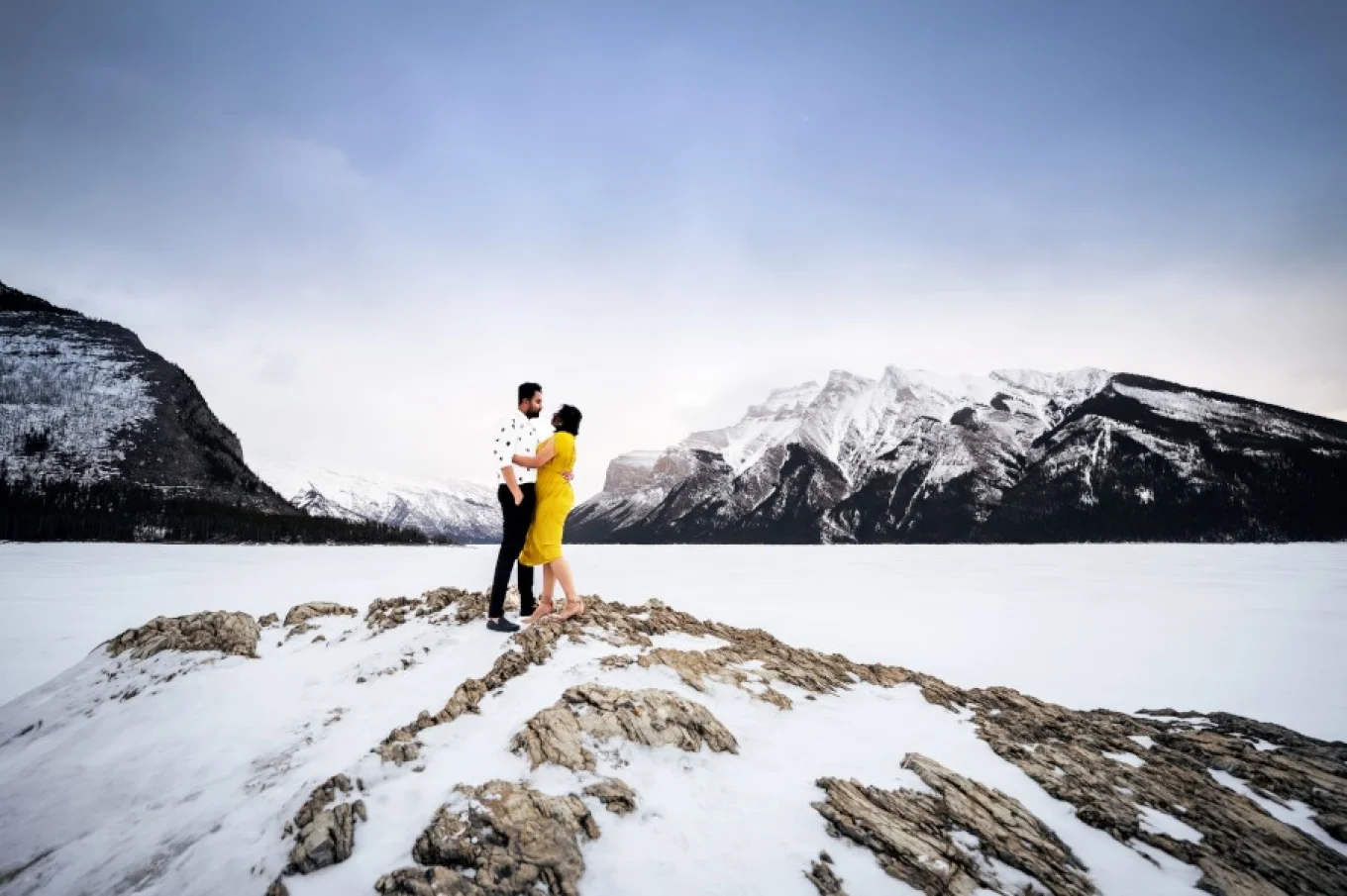Couple in love stand on island at Minnewanka Lake. during winter. They hug each other.
