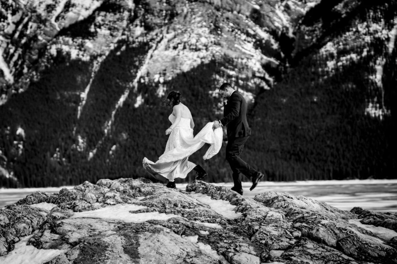Groom holds bride's wedding dress while they climb in the Canadian Rockies.