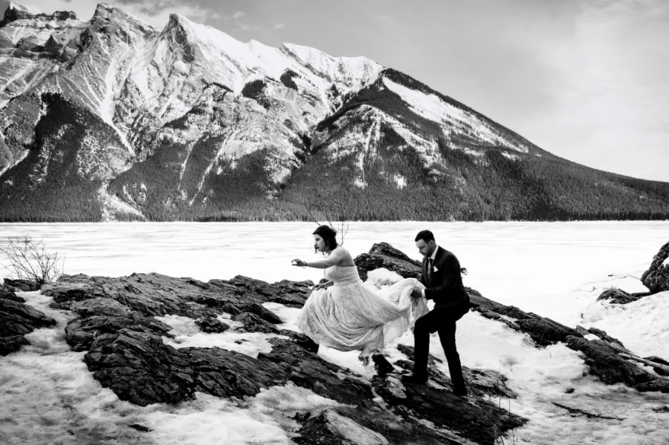Bride and groom climb the mountain during winter. Dride wears hikking boost and wedding dress.