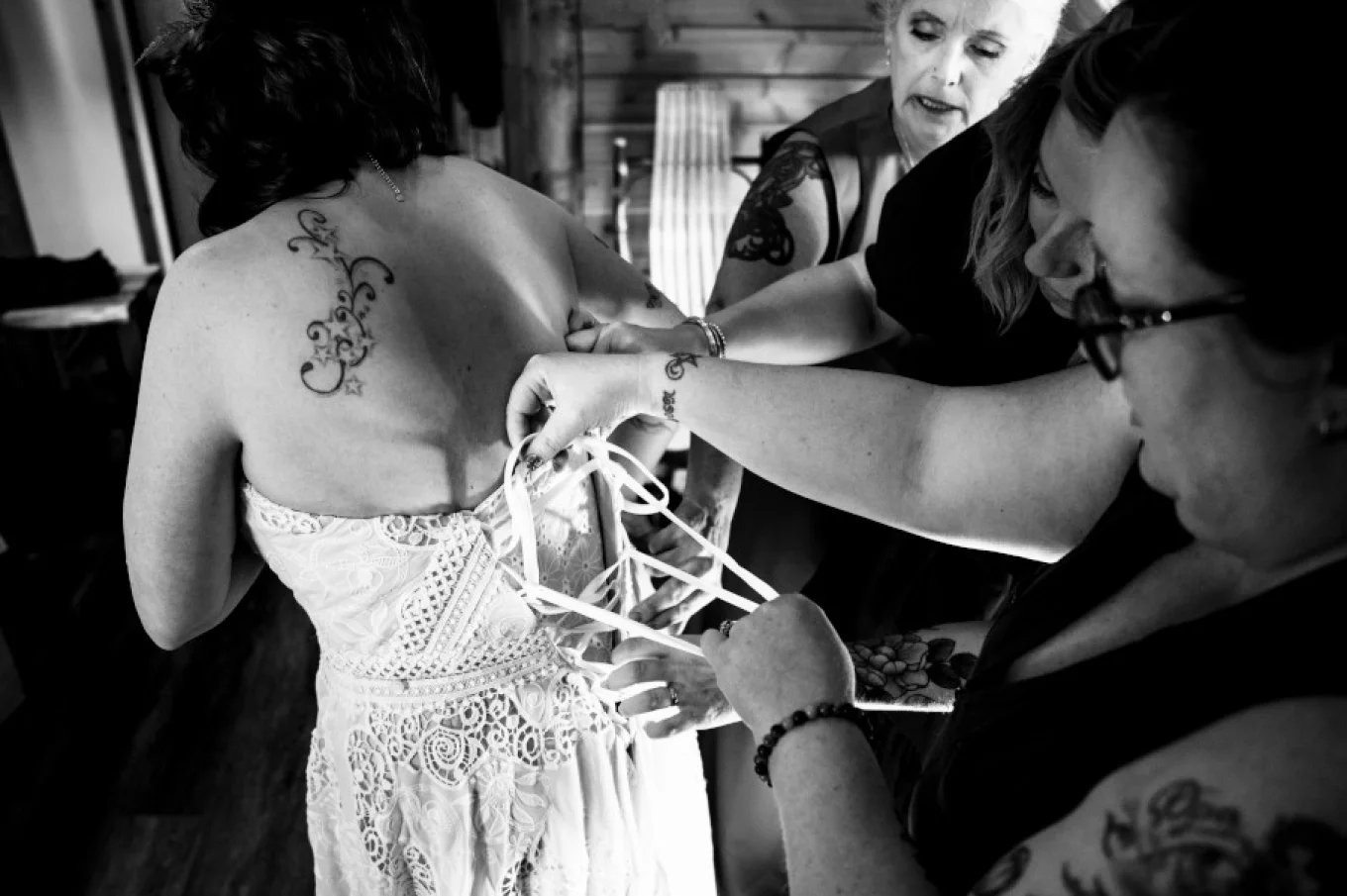 bridesmaids help bride with putting a wedding dress on.
