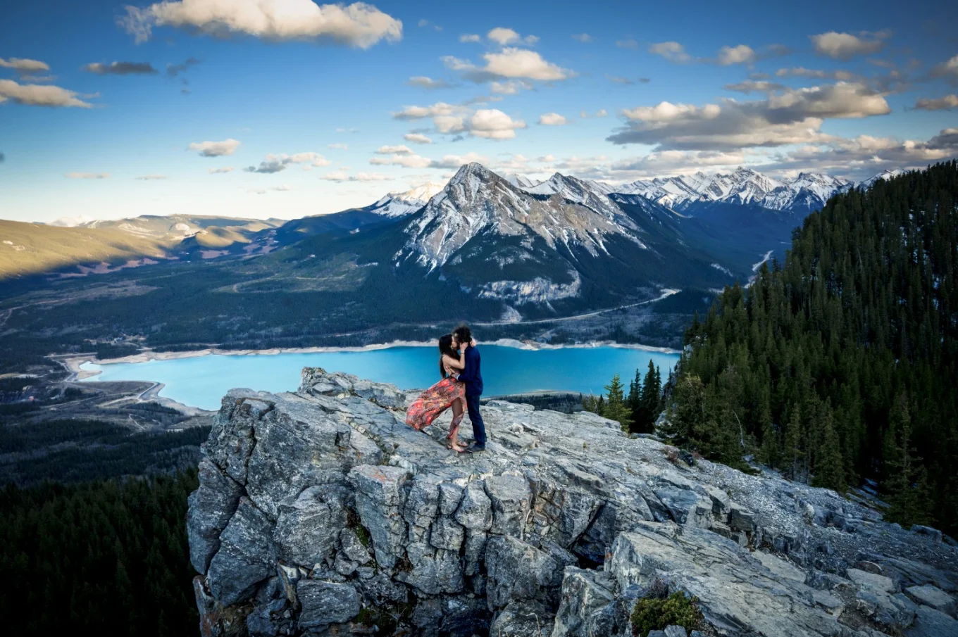 Engaged couple standing on a giant rock. On the background are Canadian Rocky Mountains and turquoise lake.