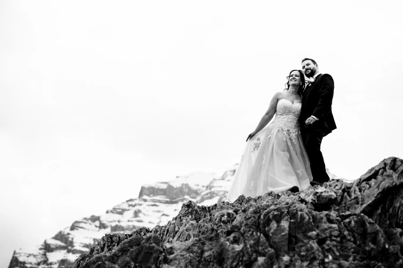 Newlyweds stand at the giant rock in the Canadian Rockies. Black and white photography captured by Calgary Wedding Photographer.