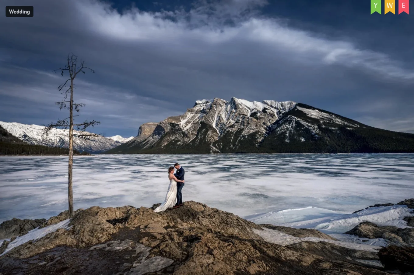 After-wedding photo of newlyweds in Banff. They hug at the frozen Minnewanka Lake.