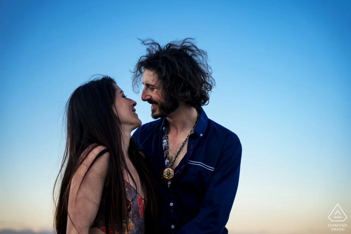 Engagement portrait of couple in love against a blue sky.