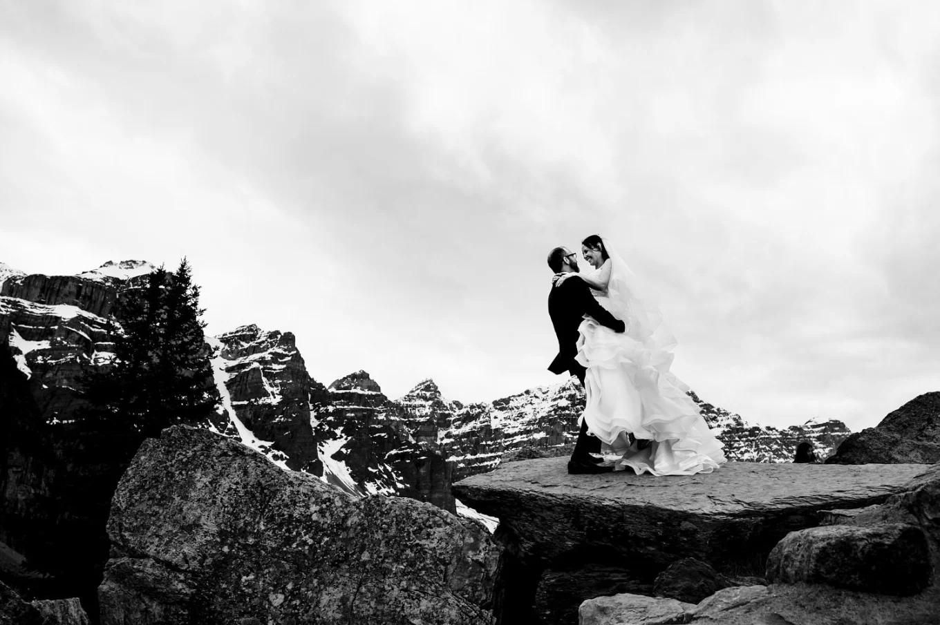 Groom lifts the bride and they both laugh during after wedding photo session at Moraine Lake