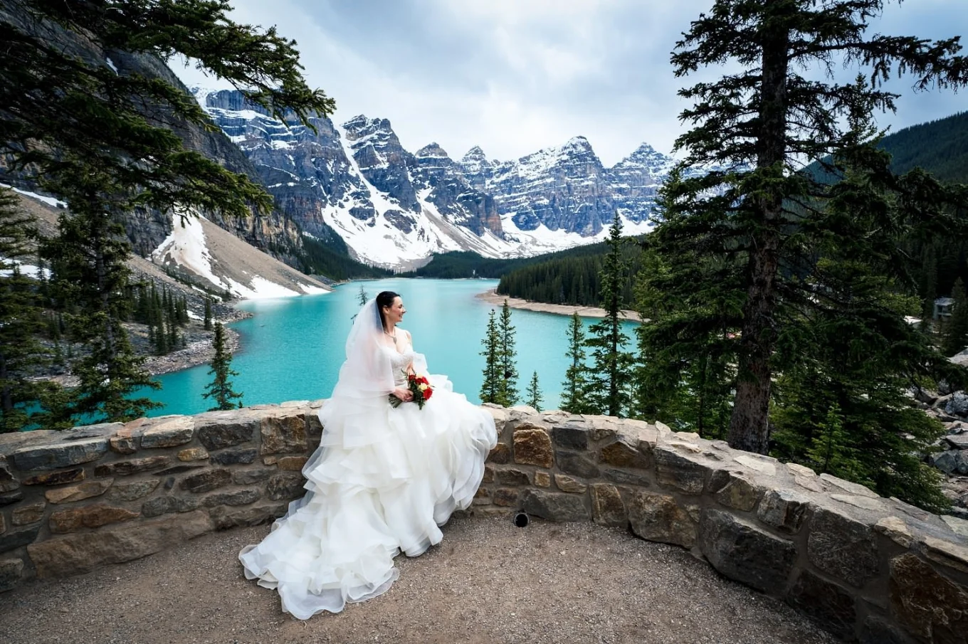 Brides portrait at Moraine Lake. She sits on the dyke against blue lake and Rocky Mountains