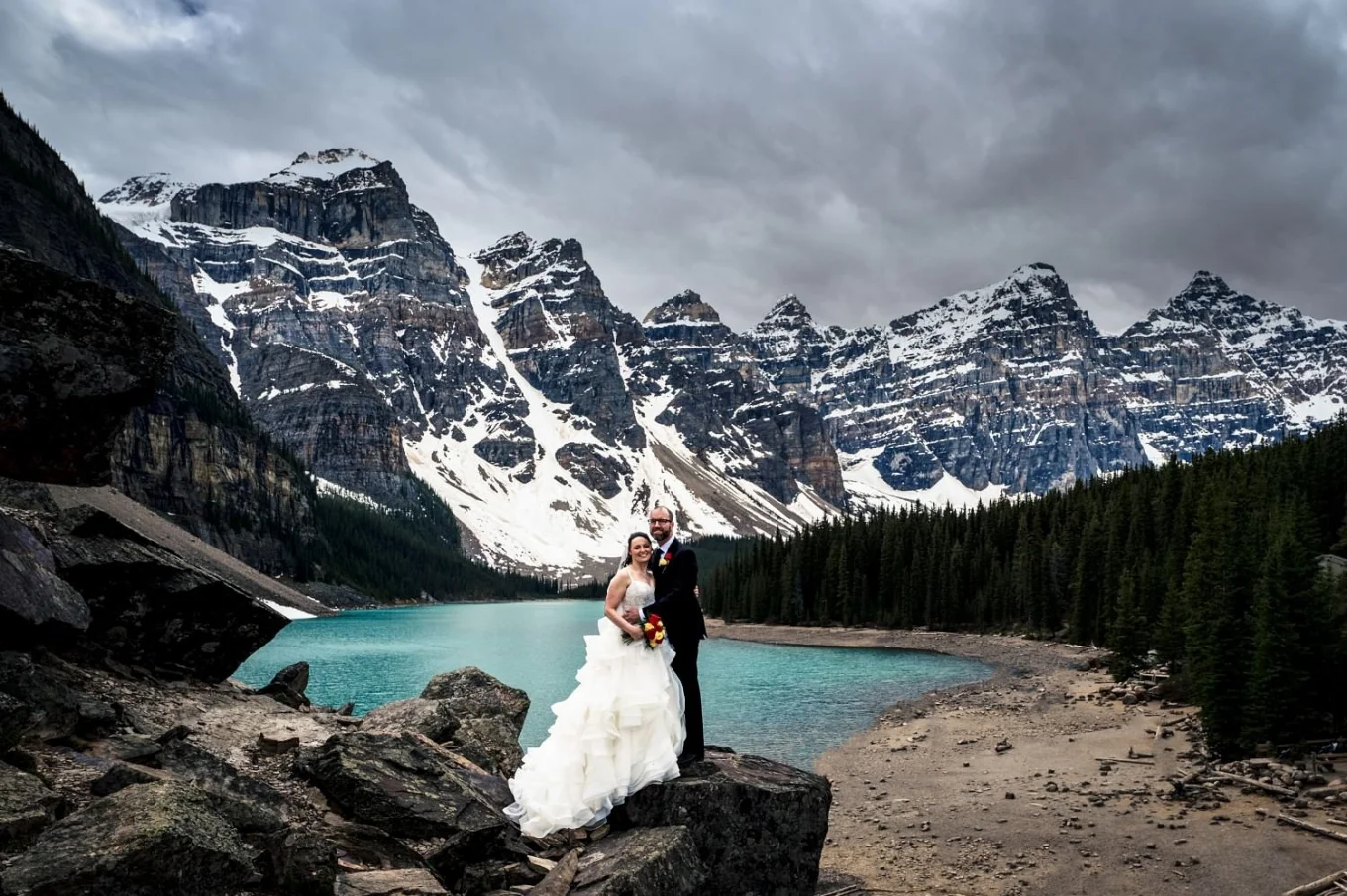 Newlyweds portrait and Moraine Lake. They are surrounded by tremendous Rocky Mountains and blue Lake.