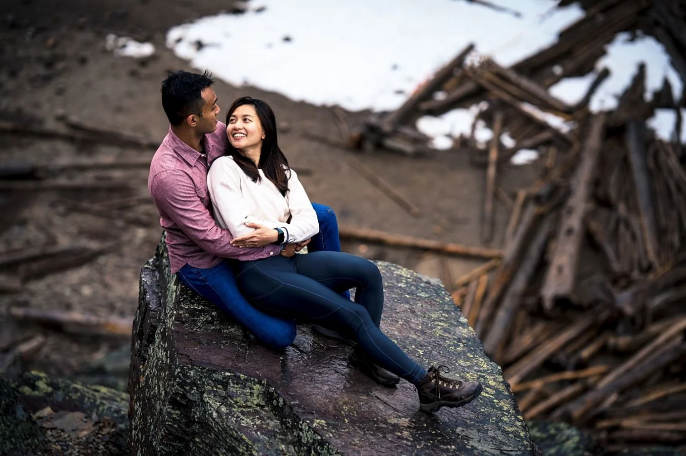 Lovely couple sit on the stone, they smile, hug and look at each others eyes.