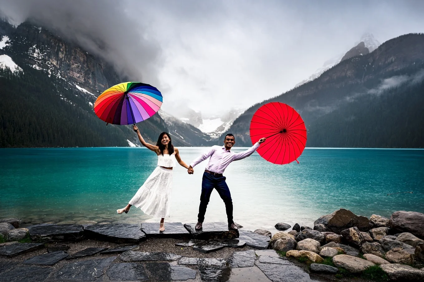 Engaged couple having fun with colourful umbrellas during an engagement, rainy photo session an Lake Louise.