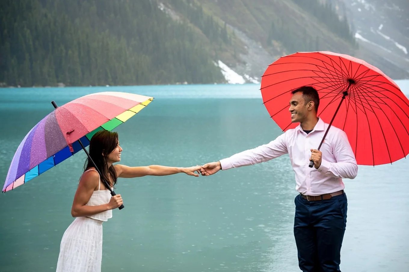 beautiful girl and handsome man hold their hands. They are under umbrellas on the rainy ray at Lake Louise.