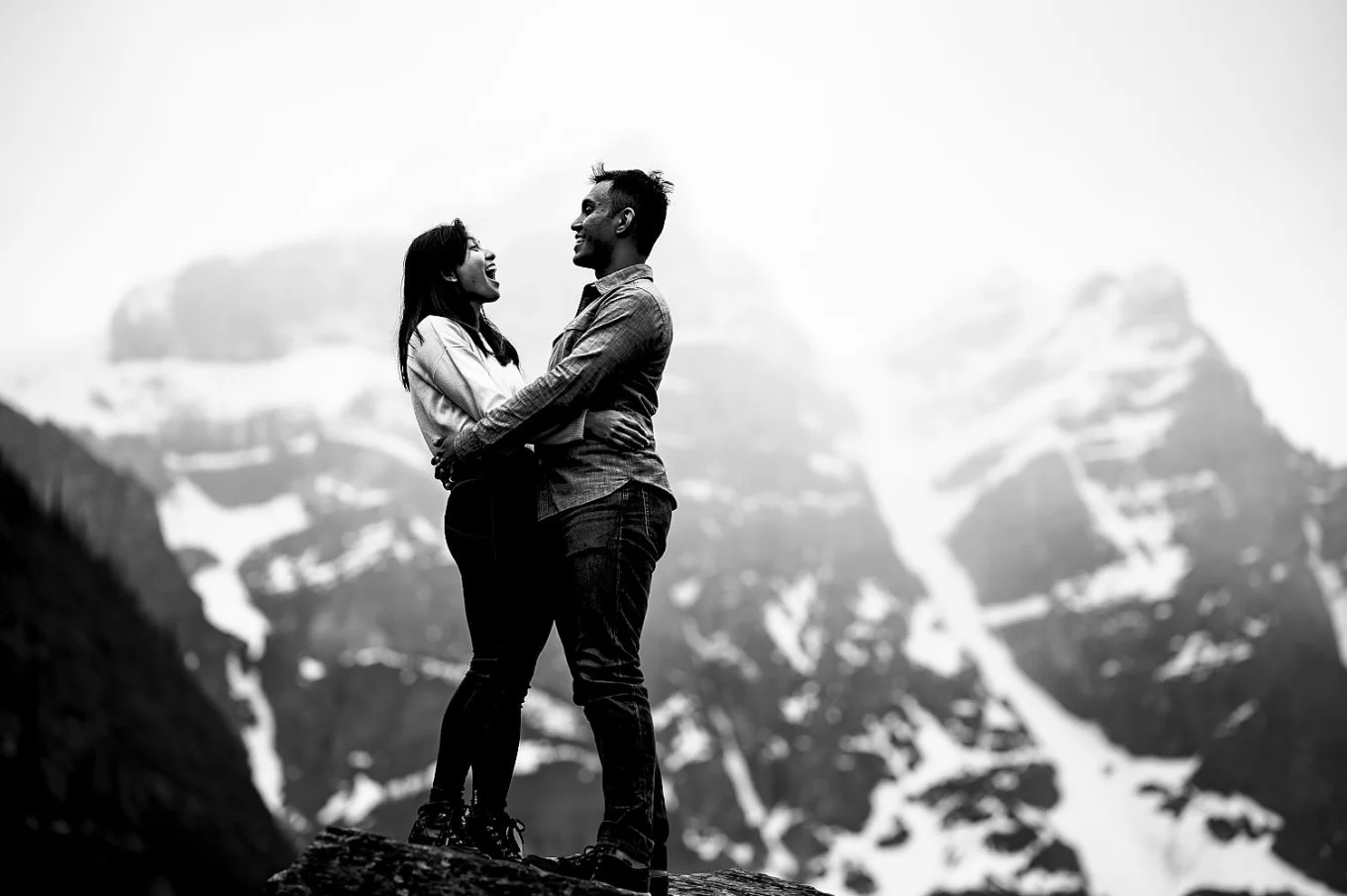 Beautiful engaged couple look at each other and laugh the snowy mountain background.