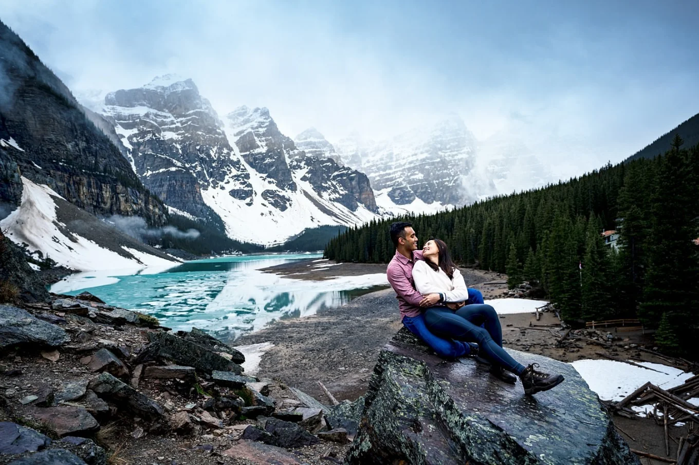 Moraine Lake engagement by the best Banff Wedding Photographer. Couple sitting at the rock over the lake.