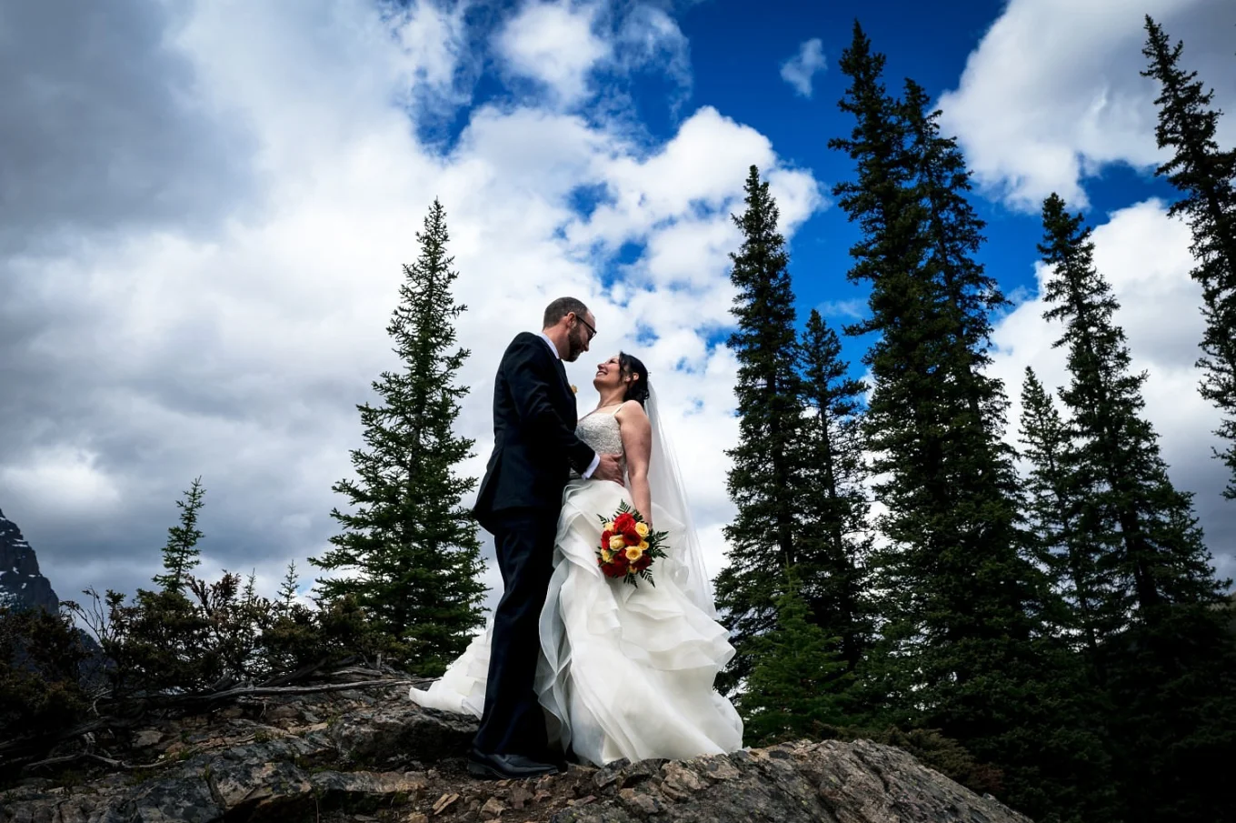 Bride and groom look at each other against a blue sky.